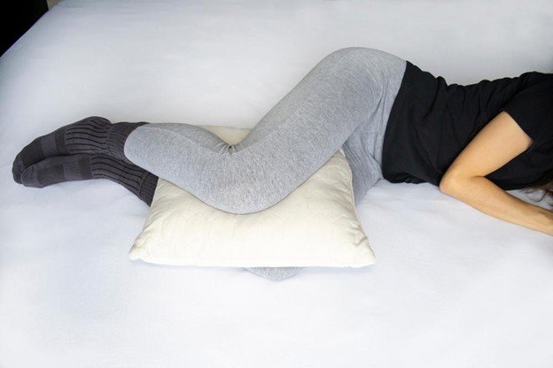 Patient placing pillow between knees for proper sleep alignment to relieve knee pain at night